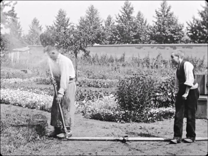 Från filmen trädgårdsmästarens hämnd (1895), Auguste & Louis Lumière. Svartvit bild av två manliga trädgårdsmästare där en får vatten i ansiktet av en slag.