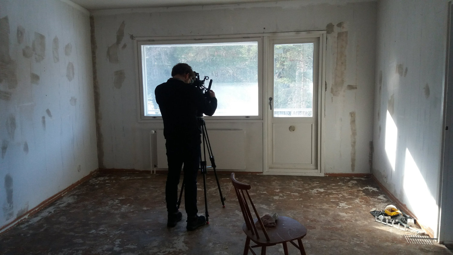 En person står med en kamera i ett rum utan möbler. Foto: Anna-Sofia Nylund.