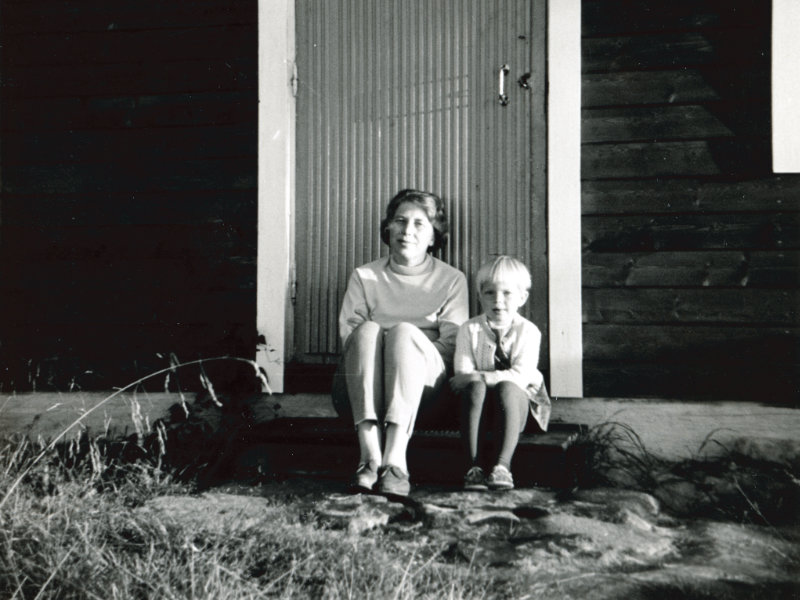 Stillbild av en kvinna och en pojke som sitter på en trappa ur filmen "Att sälja en sommarstuga". Foto: Sven Öst.