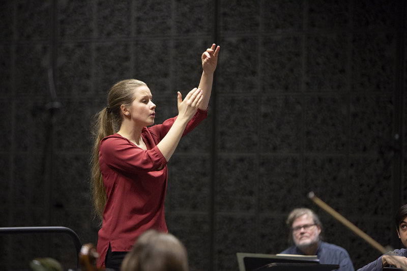 En kvinna dirigerar en orkester. Från filmen "framför orekstern". Foto Laura Oja.