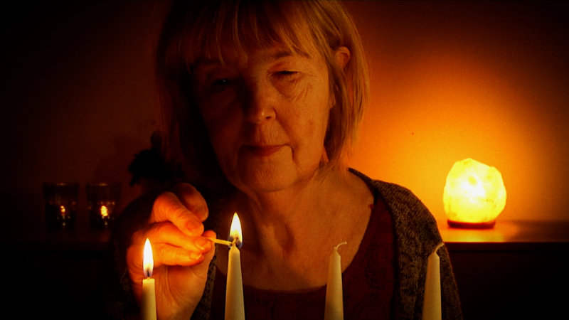 En äldre kvinna tänder ett ljus. Från filmen "Vaietut perhetarinat". Foto: Impressio films.