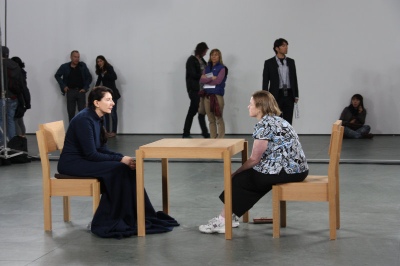 The Artist is present, Wikimedia Commons. Två personer sitter mittemot varandra vid ett bord.
