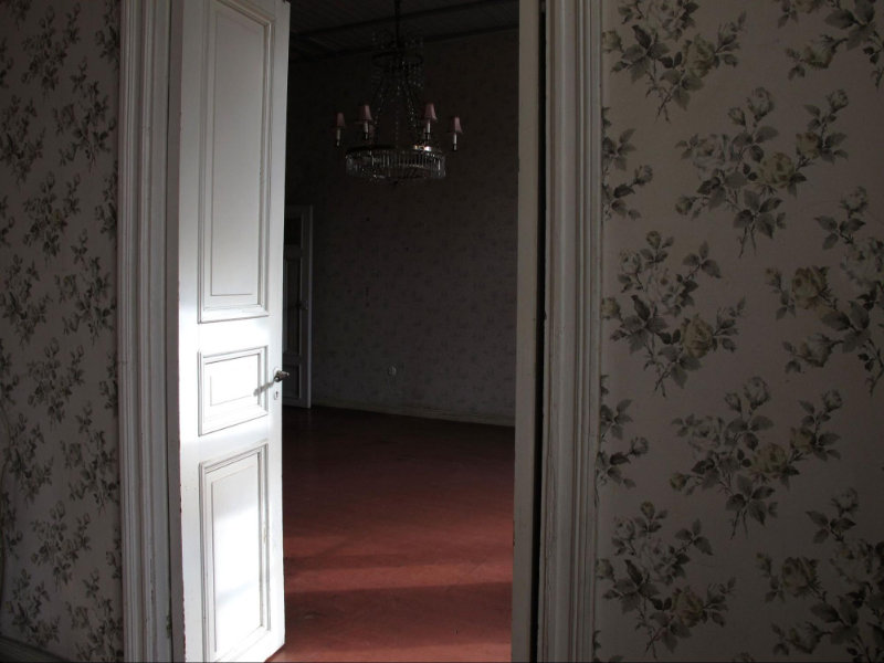 Ett rum med en dörr öppen. Stillbild från filmen "Till minne av ett hem." Foto: Helena Öst.